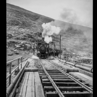 Historic steam locomotive crossing mountain trestle bridge
