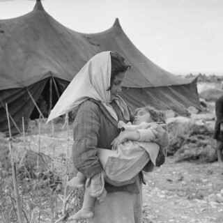 A Palestine refugee girl carries her sleeping baby sister in the newly formed Mia Mia camp, near the ancient port of Sidon, Lebanon. © 1950 UNRWA Archive Photographer Unknown Advertisement 1918-1935